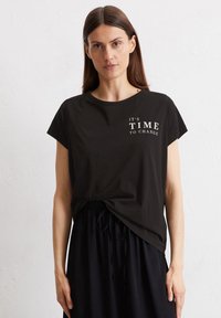 Schwarz, kurzärmliges T-Shirt aus weichem Stoff, mit einem weißen Textgrafik, die "Es ist Zeit zu ändern" zeigt. Der untere Saum ist leicht gerafft.