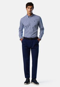 Camisa de cuadros azul con botones y mangas largas, pantalones navy y zapatillas oscuras. La camisa presenta un pequeño logo en el pecho.