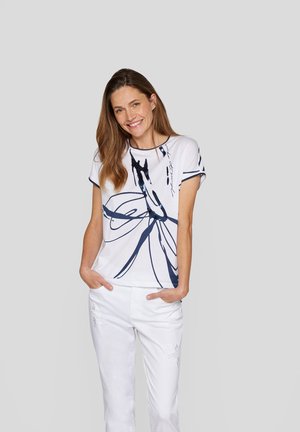 White short-sleeve t-shirt with a navy abstract floral design, featuring a round neckline and relaxed fit. Paired with white trousers.