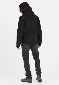 Sort vandtæt jakke med hætte, justerbare manchetter og en afslappet pasform. Båret med mørkegrå jeans og robuste støvler.