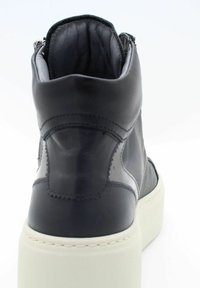 Baskets montantes en cuir noir avec semelle plateforme blanche. Présentent des coutures minimalistes et une fermeture éclair sur le côté. Texture lisse.