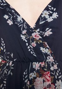 Närbild av en mörk blommig omlottklänning som visar V-ringning och sammanknuten midja med vita, rosa och röda blommönster.