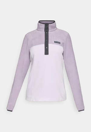 Lys lilla fleece-genser med høy krage, halvknappet front og svarte detaljer ved hals og ermer. Merkevarelogo på brystet.