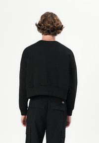 Black cropped sweatshirt with ribbed cuffs and hem, made of soft fabric. Worn with matching black cargo pants featuring back pockets.