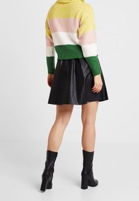 Sweter z dzianiny w żółte, różowe, białe i zielone paski; czarna spódnica z ekologicznej skóry; czarne wysokie kozaki na obcasie do kolan.