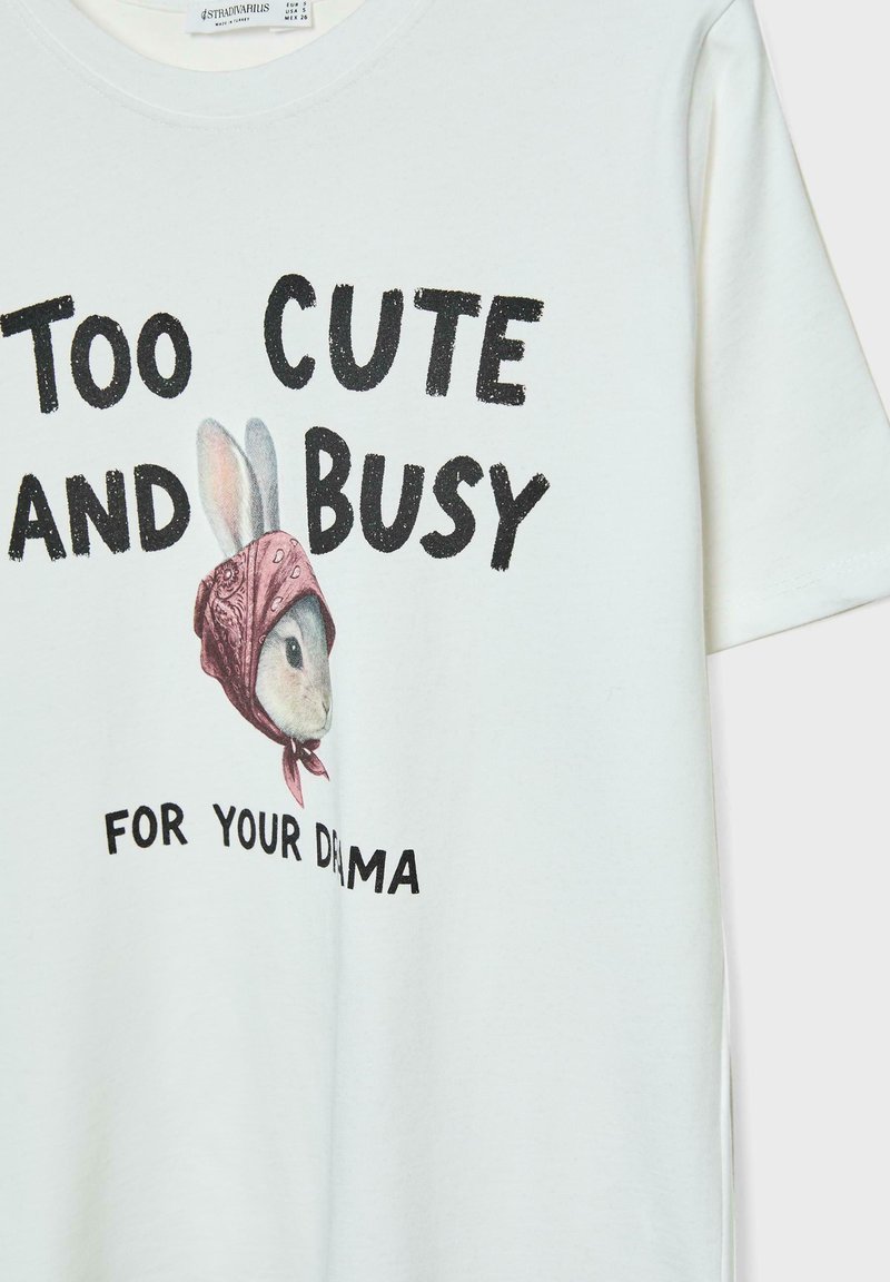 T-shirt in cotone di un leggero crema con una grafica di un coniglio che indossa un bandana rosa, con il testo "TROPPO CARINO E OCCUPATO PER LA TUA DRAMMATURGIA."
