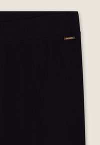 Leggings noirs avec une texture lisse, dotés d'une large taille et d'un petit logo métallique en accent. Design uni sans motifs.
