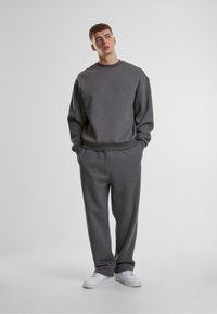 Felpa grigia e pantaloni coordinati realizzati in tessuto morbido; vestibilità comoda con polsini e cintura a coste; indossati con sneakers bianche.