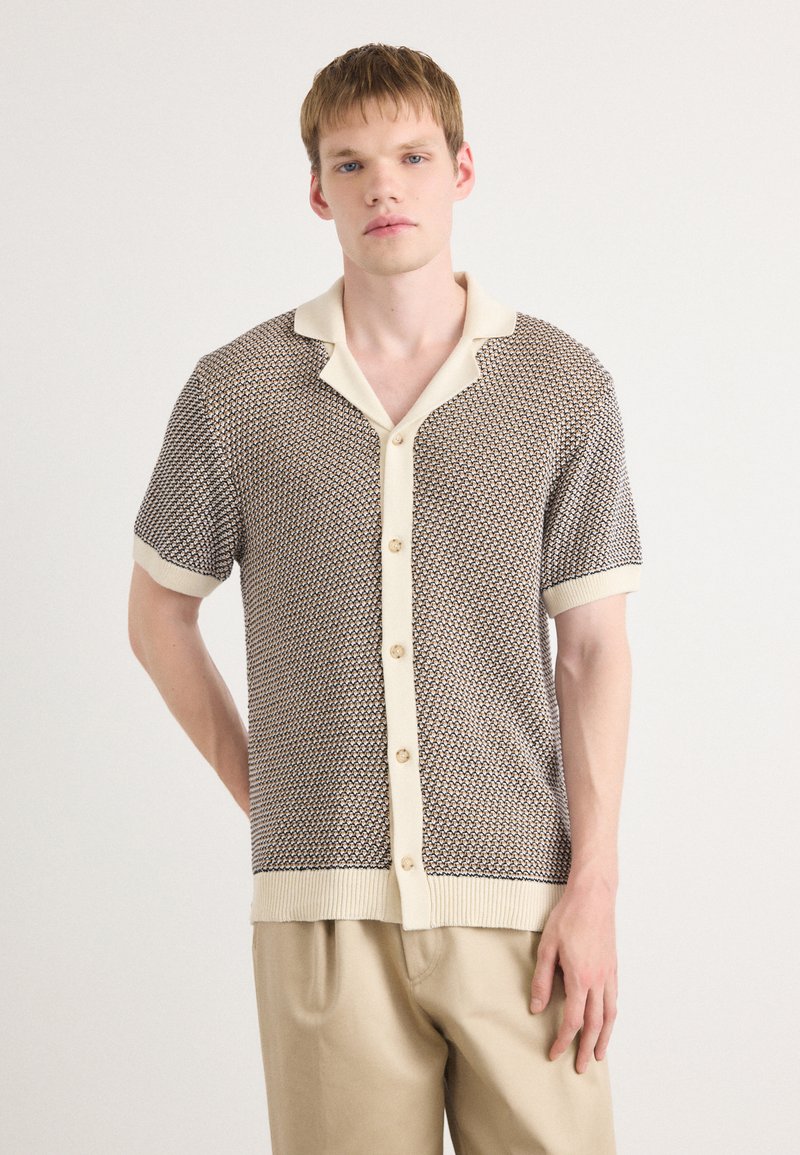 Short-sleeve knit shirt with a textured brown pattern and cream-colored collar and cuffs. Features a button-down front.