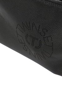 Portapenne in pelle nera texturizzata con chiusura a zip e design traforato con motivo a logo circolare. Forma compatta e minimalista.