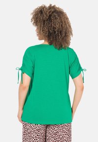 Groene short-sleeve top met een relaxte pasvorm, met strikdetails aan de mouwen. De stof is glad en past goed bij de patroonbroek.