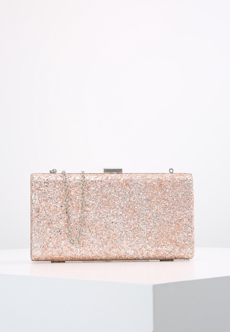 Pochette rectangulaire rose pailletée avec une bandoulière chaîne métallique et un fermoir sur un socle blanc sur fond blanc uni.