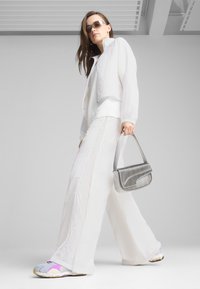 Fehér cropped dzseki, oversize fehér nadrág, színes sportcipők, szürke, textúrált felületű táska, napszemüveget viselő modell.
