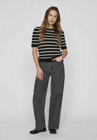 Suéter de rayas blanco y negro de manga corta combinado con vaqueros de pierna ancha grises y zapatos negros. El suéter tiene puños y bajo de canalé.