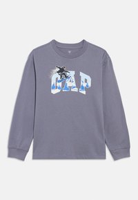 Hosszú ujjú szürke pamut póló, amelyen egy snowboardost ábrázoló grafika és a "GAP" szó látható kék-fehér színekben, bordázott mandzsettákkal.