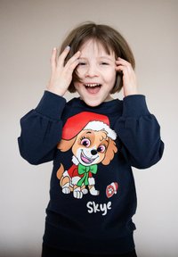 Felpa blu navy con polsini delle maniche elasticizzati, caratterizzata da un cane dei cartoni animati con un cappello di Babbo Natale, un fiocco verde e il nome "Skye" stampato sotto.
