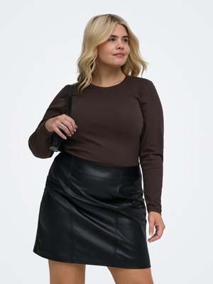 Blondínka nosiaca tmavohnedý dlhý rukáv a čiernu koženú sukňu, nesie čiernu kabelku cez rameno, pozerá sa do strany.