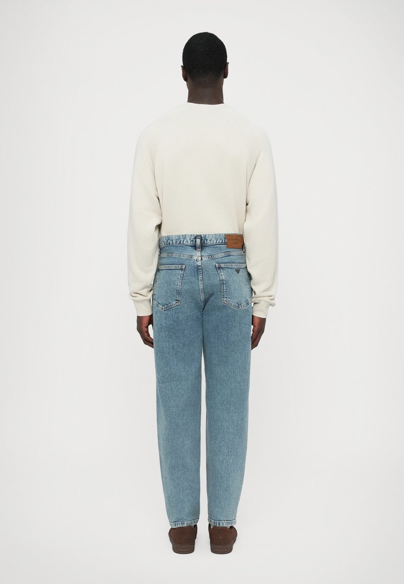 Cream sweatshirt with long sleeves, paired with light blue denim jeans. The jeans feature a leather patch at the back and a relaxed fit.