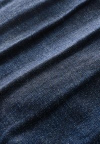 Tumedat sinised denim kangas, millel on tekstureeritud pind ja kerge sära, ning nähtav kootud muster. Kangas näitab õrnemaid voldikesi ja kortse.