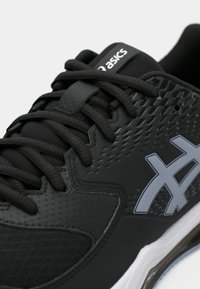 Svart sportsko med teksturert syntetisk overdel, flate svarte lisser, grå logo og en hvit såle med synlig dempeenhet.