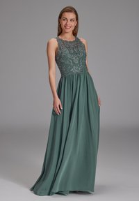 Langes türkisfarbenes Kleid mit einem Spitzen-Oberteil mit floralen Mustern, gewelltem Ausschnitt und fließendem Rock. Glatte Stoffoberfläche durchgehend.