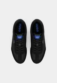 Μαύρα αθλητικά παπούτσια με λεία υφή, χαρακτηριστικό στρογγυλεμένο άκρο, μαύρα κορδόνια και μπλε λογότυπο "HUGO" στη γλώσσα και πλευρά.