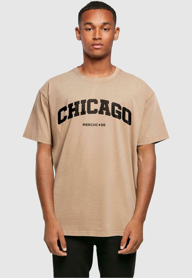 Beige puuvillat-paita, jossa on rohkeat mustat kirjaimet "CHICAGO" ja "MERCHC•DE", lyhyet hihat ja rento leikkaus.
