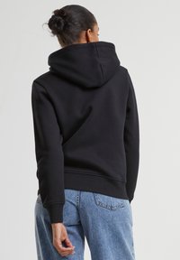 Sweatshirt à capuche noir avec une coupe décontractée, des poignets et un ourlet côtelés. Porté avec un jean taille haute bleu clair, affichant un style décontracté.