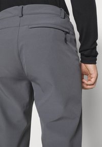 Szare spodnie z gładkiego materiału mają elastyczny pas, zasuwaną kieszeń z tyłu oraz nowoczesny krój.