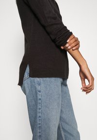 Mörkgrå stickad tröja med långa ärmar, ribbade muddar, sidoöppningar och en avslappnad passform, matchad med ljusblå högmidjade jeans.