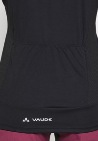 Haut de sport noir avec un panneau en maille texturée sur les côtés, une taille froncée et un logo Vaude blanc en bas.