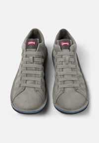 Sneaker grigi con superficie testurizzata, design con lacci e un prominente logo rosso "Camper" sulla linguetta, su uno sfondo bianco.