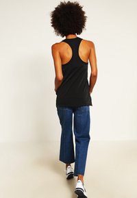 Černý bezrukávový top s designem racerback v kombinaci s modrými džínovými kalhotami a černobílými teniskami.