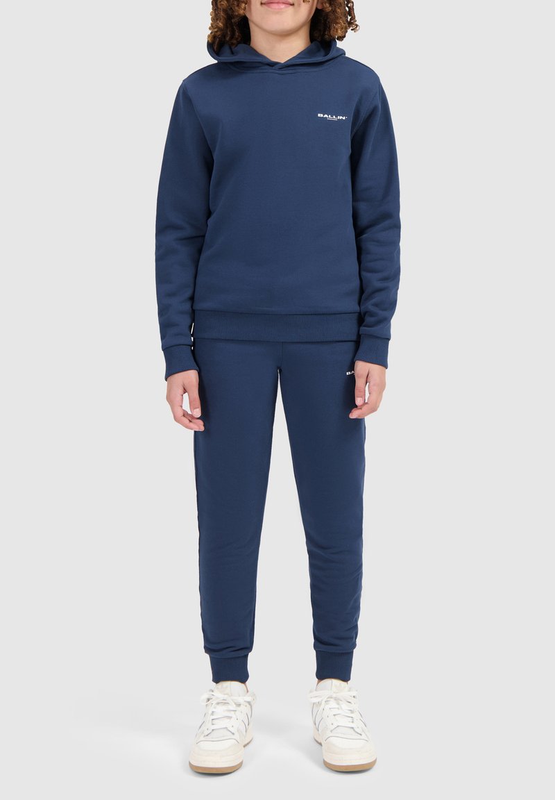 Navyblauwe sweatshirt en joggingsbroek van zachte stof; mouwen van gemiddelde lengte, ribgebreide boorden en een klein logo op de borst en het been.