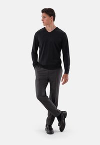 Dunkelgrauer V-Ausschnitt-Pullover kombiniert mit hellgrau gemusterten Anzughosen und schwarzen Loafers, mit einer eleganten Silhouette und glatten Texturen.