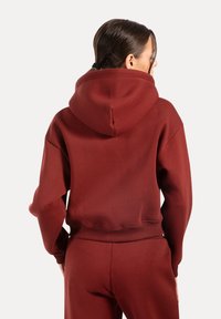 Burgundowa bluza z obszernym kapturem, ściągaczami na mankietach i dolnym brzegu. Miękka tekstura, luźny krój i minimalistyczny design. Noszona z dopasowanymi spodniami.