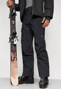 Μαύρο σκι παντελόνι με υφή, τσέπες με φερμουάρ, ενισχυμένα κάτω μέρη στα πόδια. Σκι με δεσίματα, μαύρα μπότες σκι με πράσινες λεπτομέρειες.