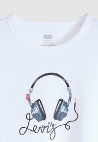 Λευκό t-shirt Levi's με σχέδιο μπλε ακουστικών και μαύρο καλώδιο που σχηματίζει τη λέξη "Levi's" κάτω από την ετικέτα στον γιακά.