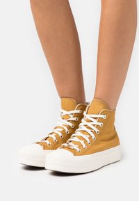 High-top sneakers in mustard yellow canvas with white laces, round toe, rubber sole, and textured accents.
