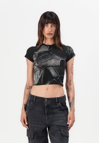 Black cropped t-shirt featuring a denim pattern, round neckline, and short sleeves, paired with high-waisted dark cargo pants with pockets.
