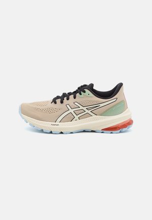 Beiger und hellgrüner Laufschuh mit schwarzen Schnürsenkeln, gepolsterter Sohle mit orangefarbenem Fersenbereich und seitlichem Logo auf weißem Hintergrund.