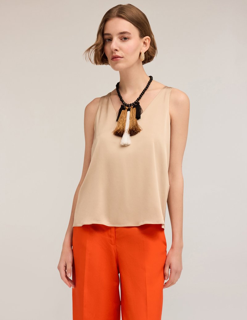 Top sin mangas beige con una textura suave, combinado con pantalones naranja brillante. Un collar llamativo con flecos negros y dorados adorna el escote.