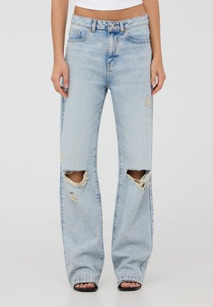 Jeans azzurri chiari a vita alta con una vestibilità rilassata, caratterizzati da strappi evidenti sulle ginocchia, bordi sfilacciati e una leggera scoloritura in tutto il tessuto.