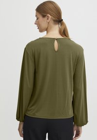Olivengrønn langermet topp med rund hals, samlet puff-sleeves og en n�økkelhulldetalj bak, laget av mykt stoff.
