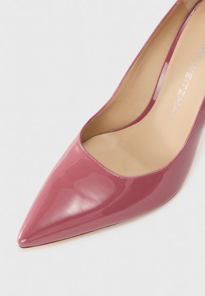 Pink patent leather high heel shoe with a pointed toe and a curved opening, featuring a beige interior lining and subtle branding.