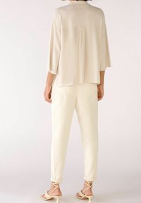 Světlý béžový pruhovaný top s netopýřími rukávy, doplněný krémovými kalhotami s volným střihem a ohrnutými manžetami. Sandály na řemínky v tělové barvě.