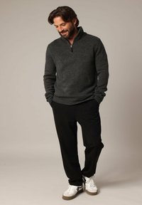 Un pull zippé gris foncé avec une finition texturée, associé à un pantalon noir et des baskets blanches avec des accents noirs et verts.