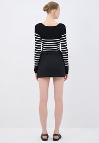 Maglione a righe in bianco e nero con maniche lunghe abbinato a una gonna corta nera. Tessuto liscio, design aderente e senza motivi o decorazioni visibili.
