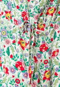 Tessuto a fantasia floreale con fiori rossi, gialli e viola su uno sfondo verde chiaro; include un dettaglio con lacci in vita.
