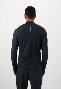 Langærmet sort atletisk top med teksturerede stribede ærmer og en reflekterende detaljeret linje på ryggen. Fremstillet af strækbart materiale.